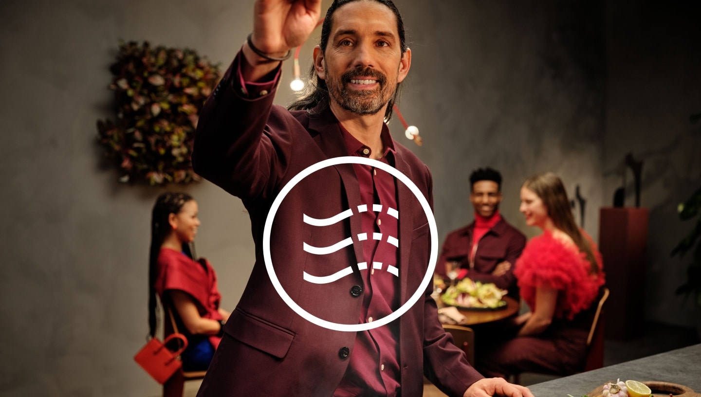 Крупно изображение на мъж на вечеря с гости, седнали на маса на заден план.