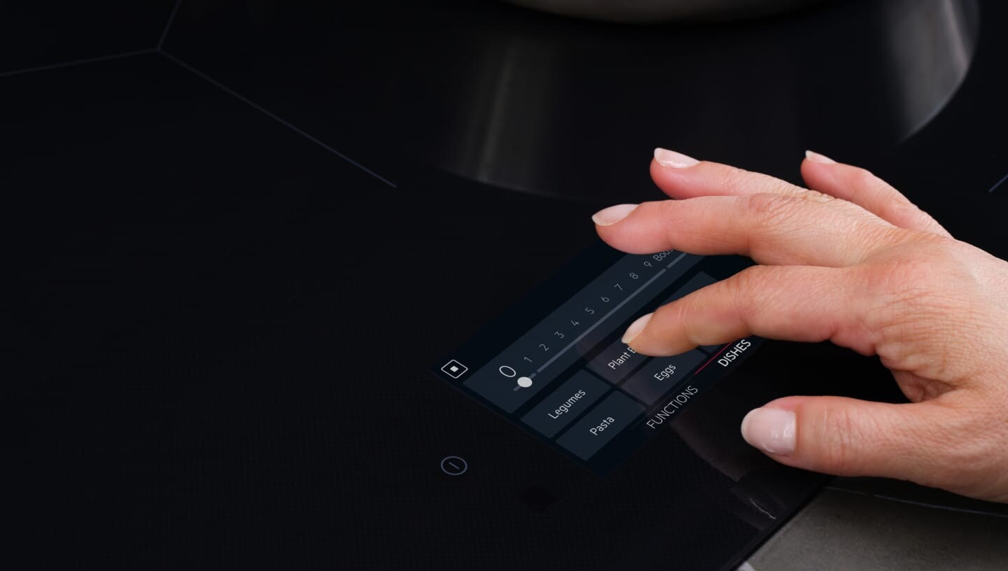 Пръст се допира до контролния панел на индукционен плот.