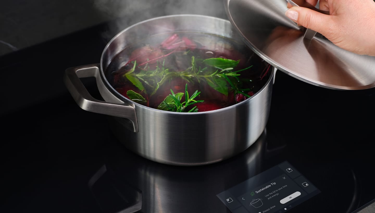 Една ръка сваля капака на тенджерата с врящи зеленчуци.