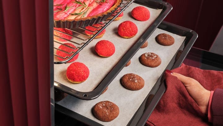 Човек поставя няколко тави с десерти във фурната