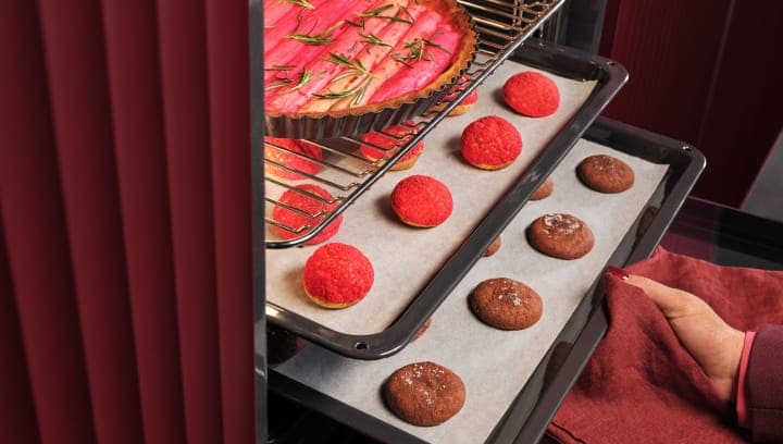 Човек изважда тава с печива от фурната.