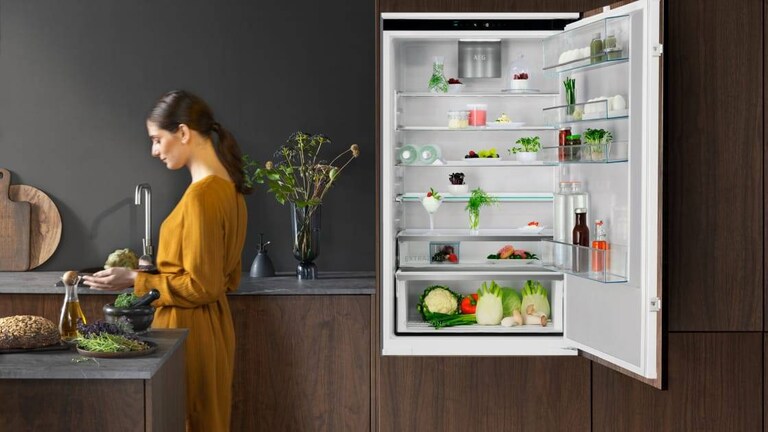 Жена стои в кухня с отворена врата на хладилник